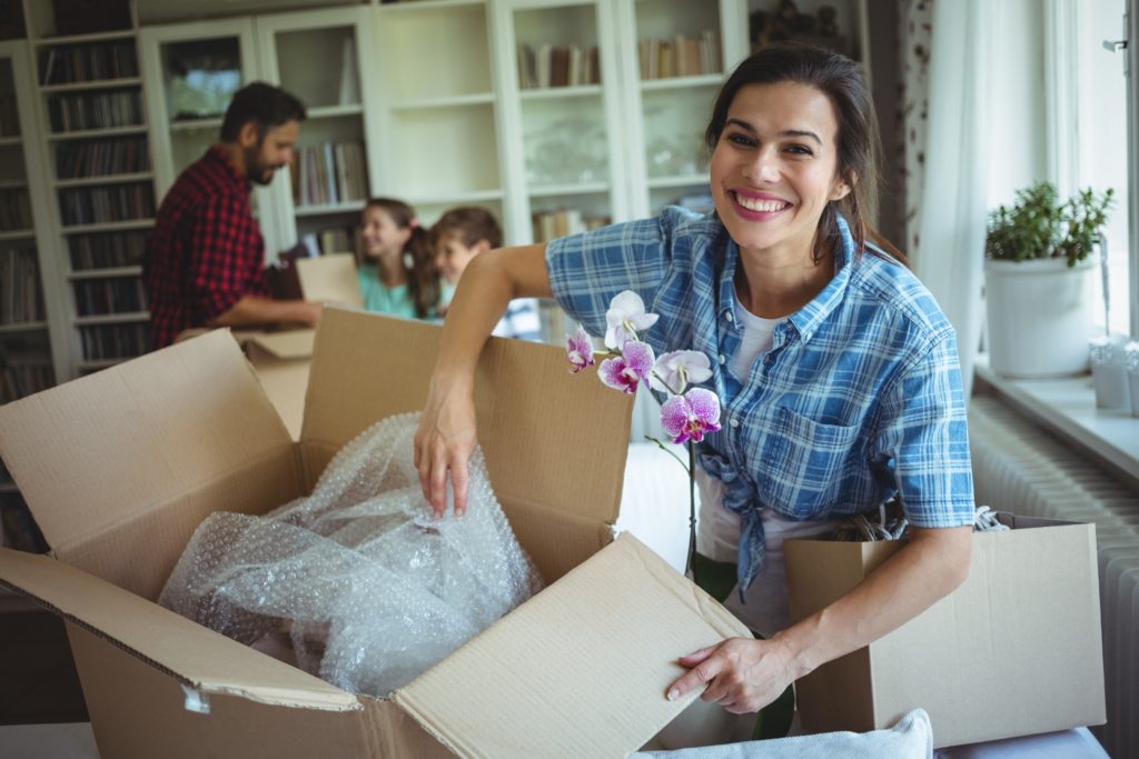 A woman is smiling and unpacking boxes while her family rejoices in the background after finding the best moving company in Murfreesboro, Tennessee.